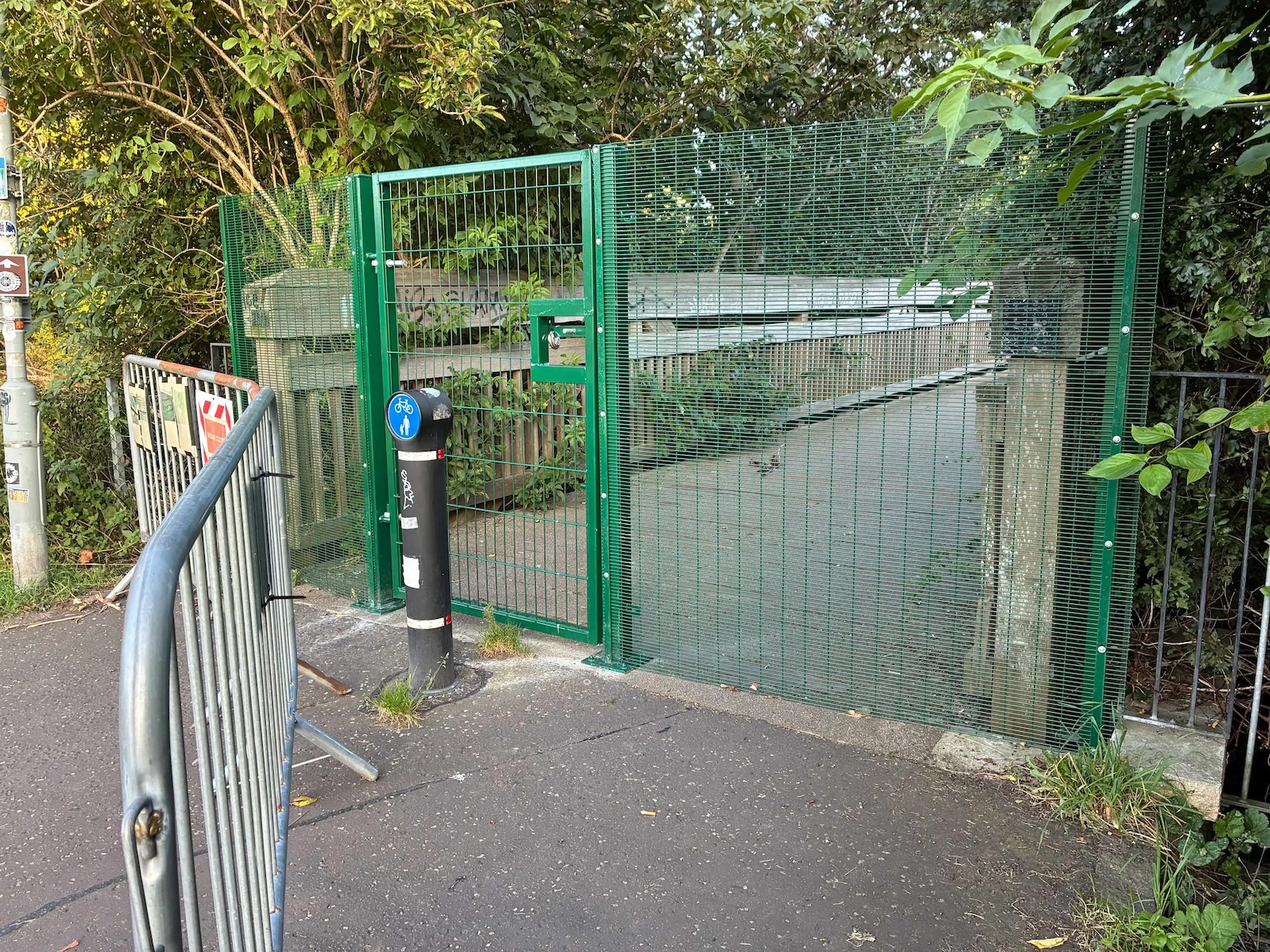 A green fence with doorway across a wooden footbridge in a green park